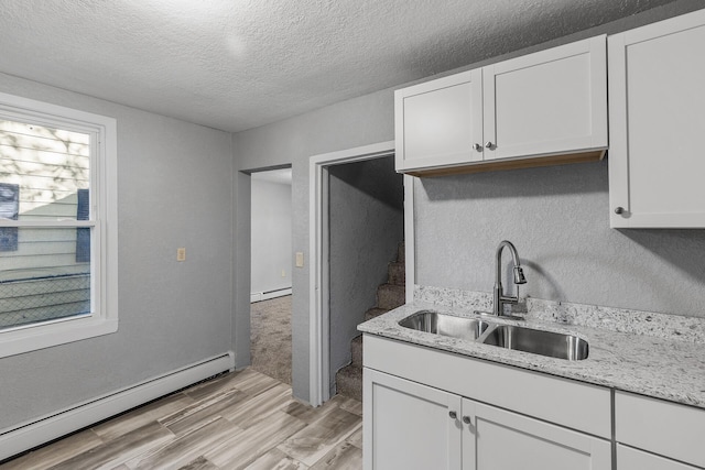 kitchen featuring white cabinets, baseboard heating, sink, and light wood-type flooring