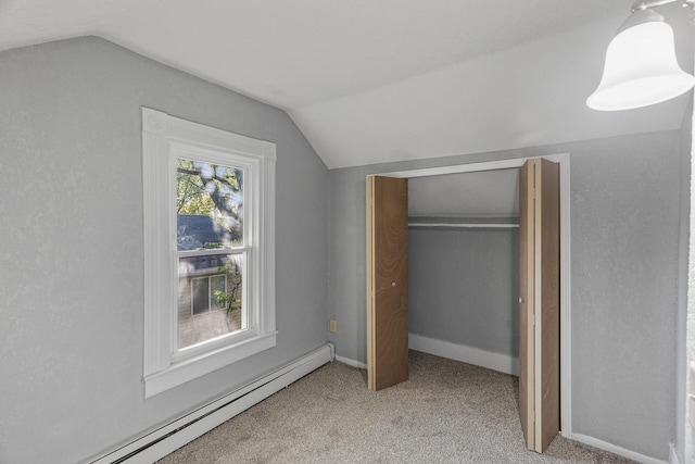 unfurnished bedroom with lofted ceiling, a closet, a baseboard heating unit, and carpet