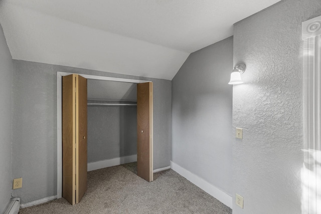 unfurnished bedroom with lofted ceiling, a closet, a baseboard heating unit, and light carpet