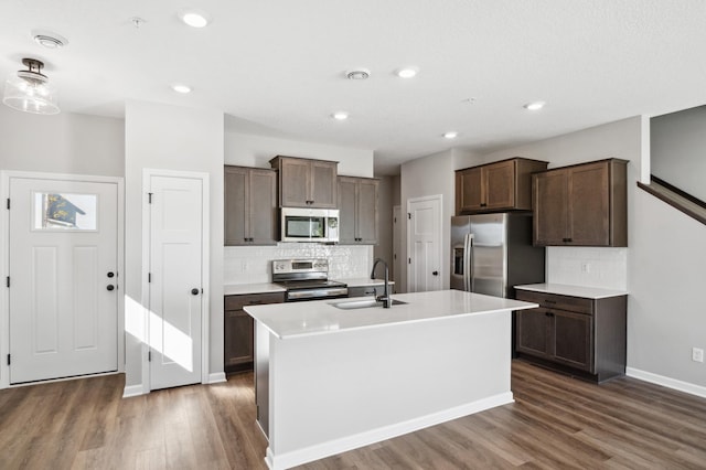 kitchen with dark brown cabinets, dark wood-type flooring, a center island with sink, sink, and stainless steel appliances