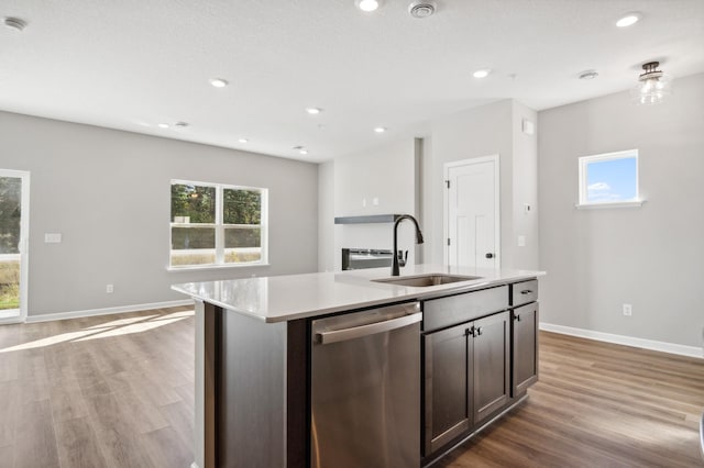 kitchen with a kitchen island with sink, dark brown cabinets, sink, dishwasher, and hardwood / wood-style flooring