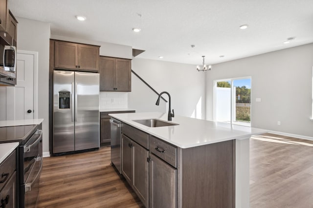 kitchen featuring a kitchen island with sink, decorative light fixtures, sink, dark hardwood / wood-style floors, and appliances with stainless steel finishes