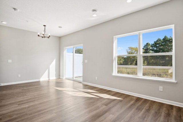 empty room featuring wood-type flooring, a chandelier, and a healthy amount of sunlight