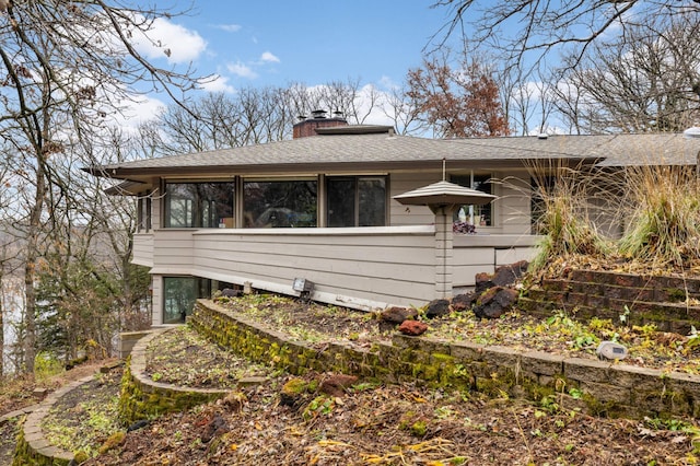 view of side of property featuring a shingled roof and a chimney