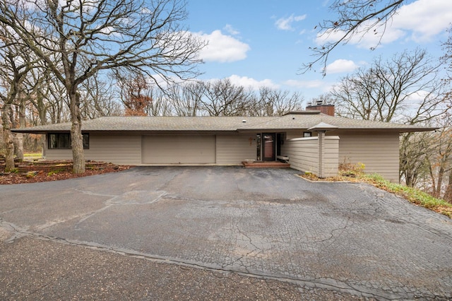 view of front of house with aphalt driveway, a chimney, and an attached garage