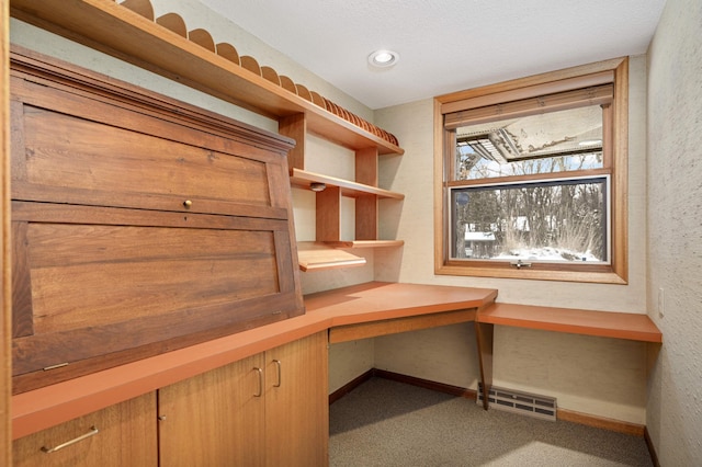 unfurnished office with a textured wall, built in desk, carpet flooring, and visible vents