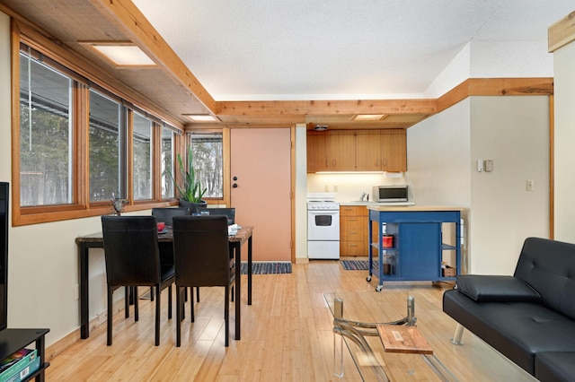 kitchen with white range with electric cooktop, light wood-style flooring, light countertops, brown cabinets, and stainless steel microwave