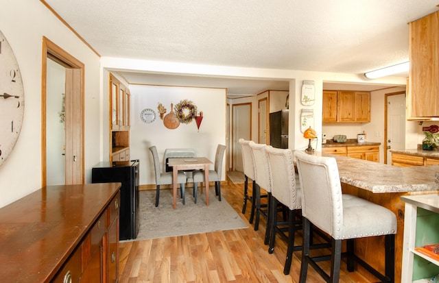 kitchen with a kitchen bar, a textured ceiling, and light hardwood / wood-style flooring