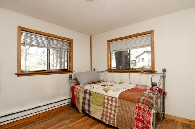 bedroom with a baseboard radiator, a textured ceiling, and wood finished floors