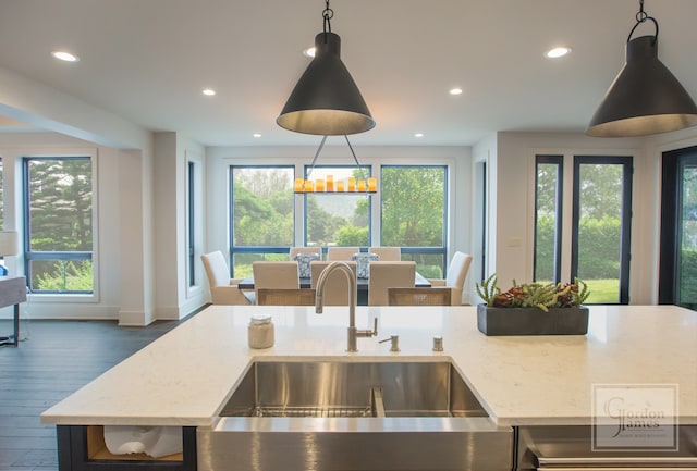 kitchen with a kitchen island with sink, dark hardwood / wood-style flooring, sink, light stone countertops, and hanging light fixtures