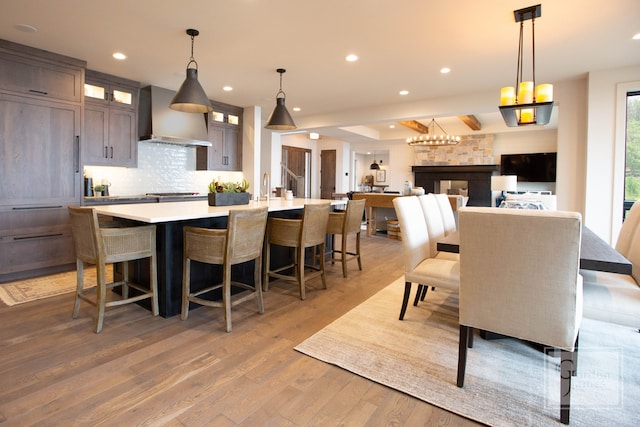 kitchen featuring wall chimney range hood, light hardwood / wood-style floors, decorative light fixtures, and a large island