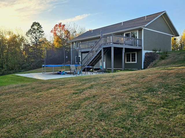 back house at dusk featuring a trampoline, a yard, and a deck