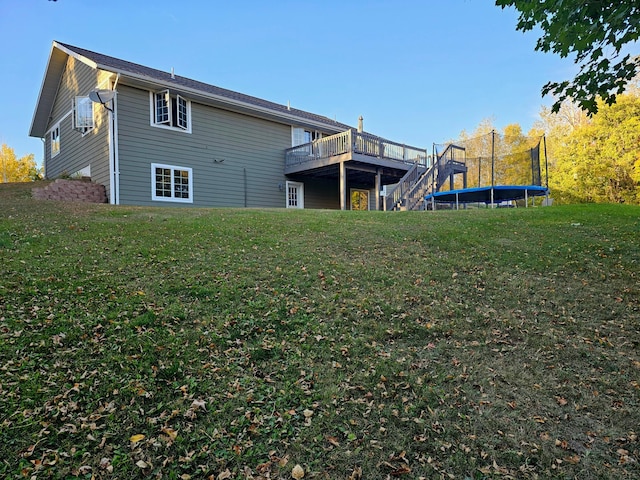 back of house with a trampoline, a wooden deck, and a yard