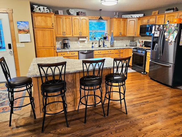 kitchen with a kitchen island, a textured ceiling, light hardwood / wood-style flooring, backsplash, and black appliances