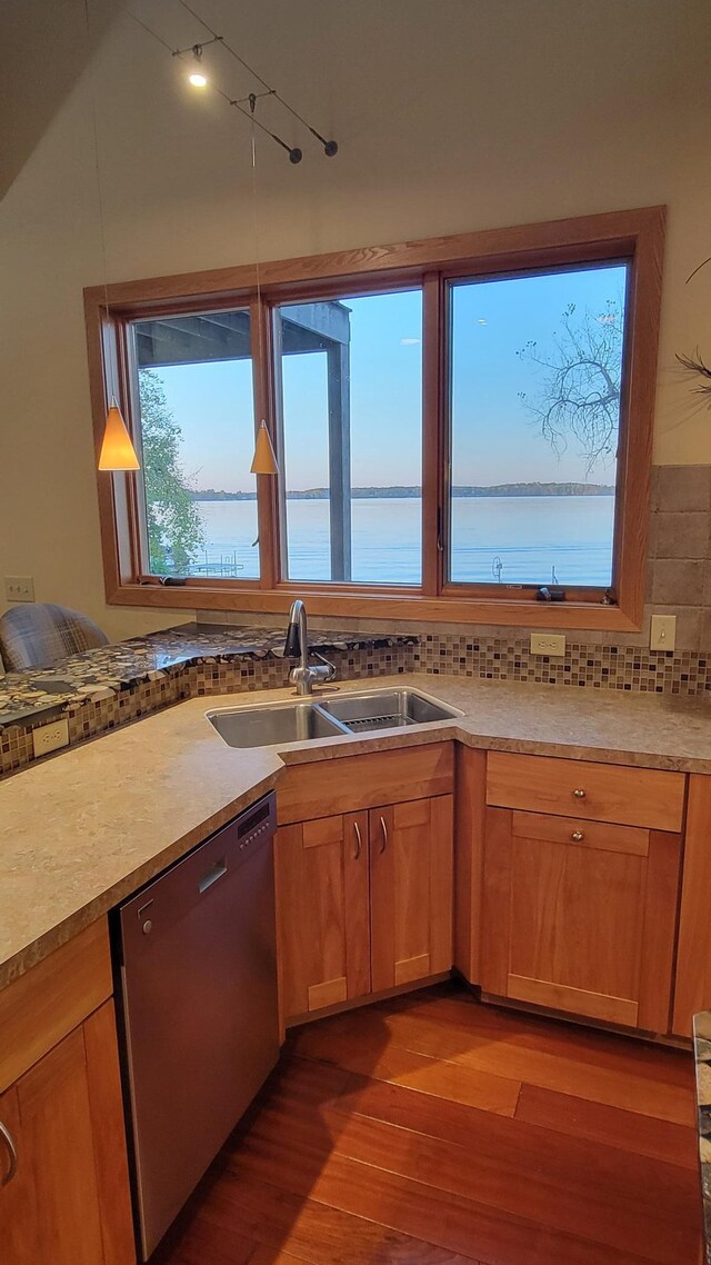 kitchen featuring sink, hardwood / wood-style floors, pendant lighting, stainless steel dishwasher, and a water view