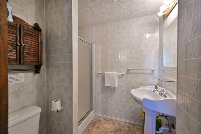 bathroom with toilet, a textured ceiling, tile walls, and a stall shower