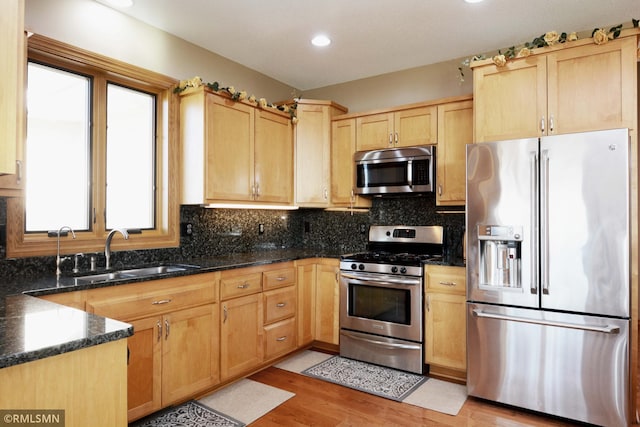 kitchen with tasteful backsplash, appliances with stainless steel finishes, sink, dark stone countertops, and light hardwood / wood-style flooring