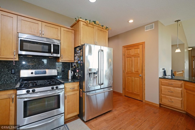 kitchen with decorative backsplash, hanging light fixtures, dark stone countertops, light hardwood / wood-style floors, and stainless steel appliances