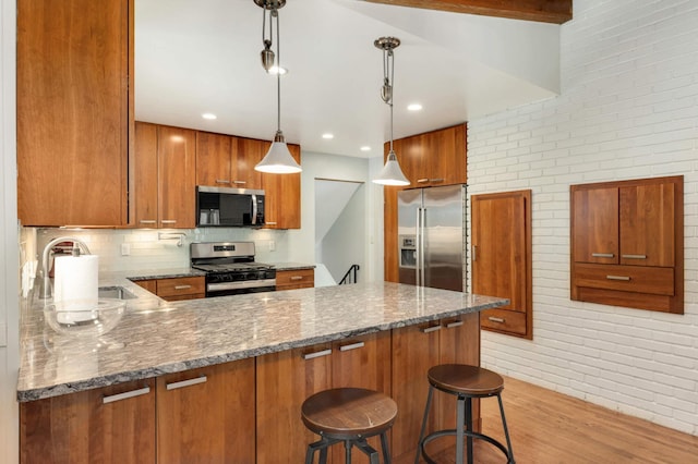 kitchen featuring dark stone countertops, sink, stainless steel appliances, hanging light fixtures, and a breakfast bar area