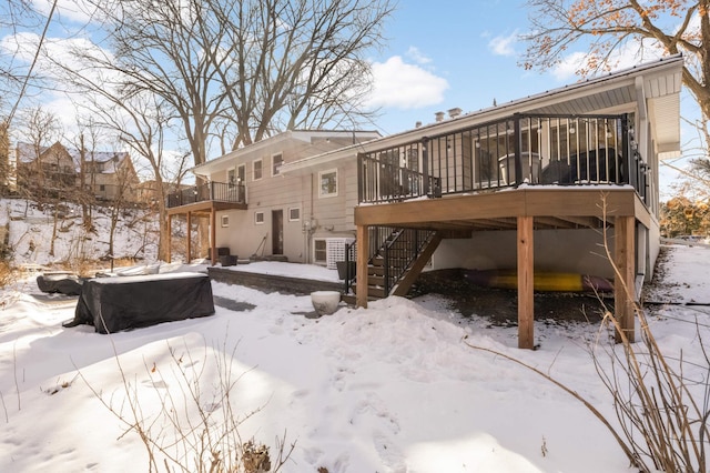 snow covered rear of property featuring a sunroom and a wooden deck