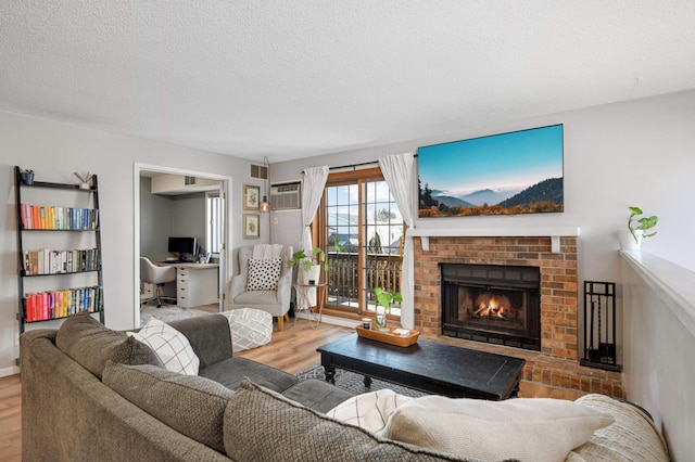 living room featuring a brick fireplace, a textured ceiling, light hardwood / wood-style flooring, and an AC wall unit