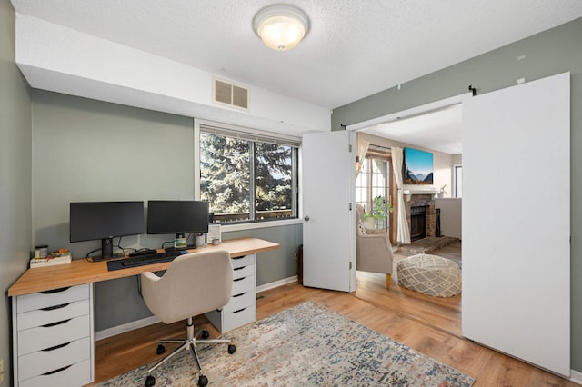 office with light hardwood / wood-style floors, a textured ceiling, and a brick fireplace