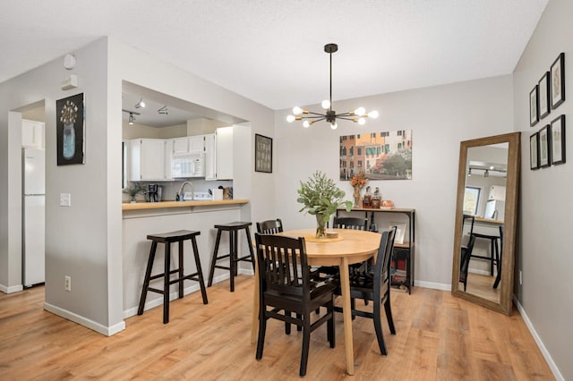 dining area with ceiling fan with notable chandelier, light hardwood / wood-style flooring, and sink