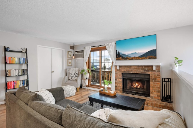 living room with a wall mounted air conditioner, hardwood / wood-style floors, a textured ceiling, and a brick fireplace