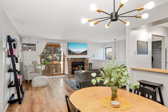 dining room with an inviting chandelier, an AC wall unit, a textured ceiling, a fireplace, and light hardwood / wood-style floors