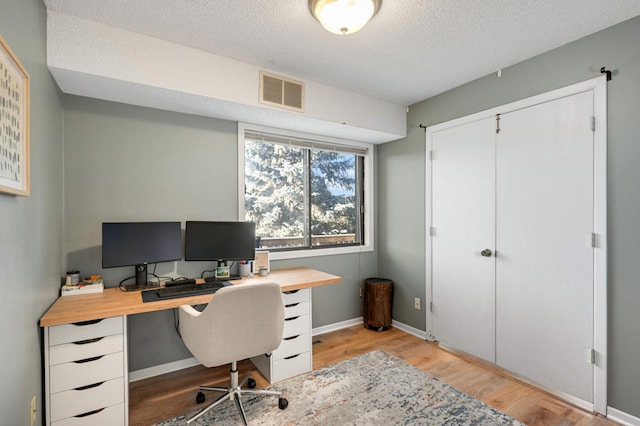 home office with a textured ceiling and light hardwood / wood-style floors