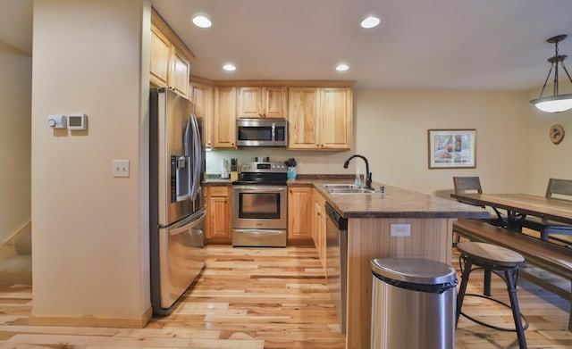 kitchen with light wood-type flooring, pendant lighting, light brown cabinetry, sink, and stainless steel appliances