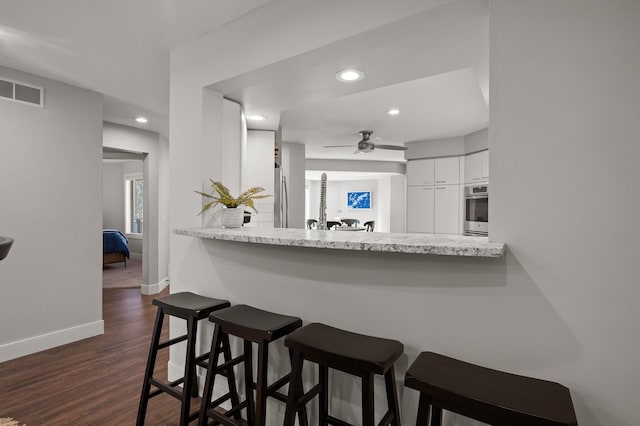 kitchen featuring kitchen peninsula, white cabinetry, stainless steel appliances, dark hardwood / wood-style floors, and a kitchen bar