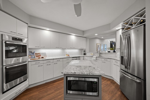 kitchen featuring decorative backsplash, a kitchen island, dark wood-type flooring, stainless steel appliances, and white cabinetry