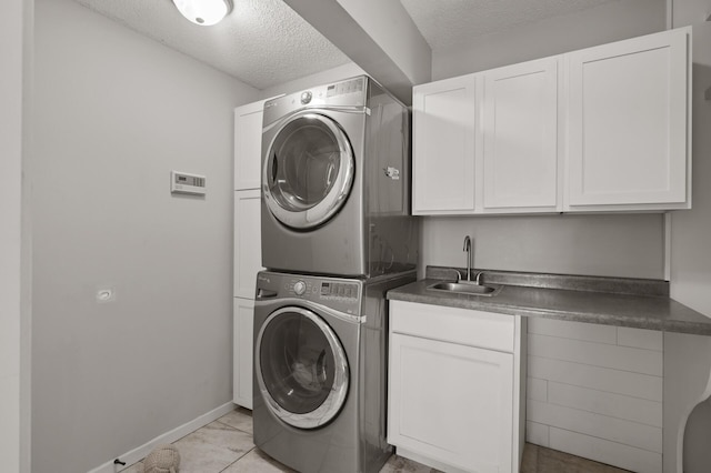 laundry room with stacked washing maching and dryer, cabinets, sink, light tile patterned floors, and a textured ceiling