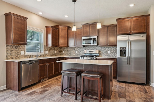 kitchen with appliances with stainless steel finishes, hanging light fixtures, dark wood-type flooring, and a kitchen island