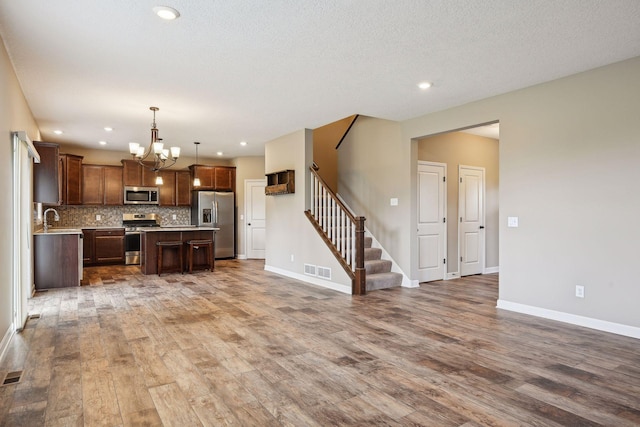 kitchen featuring wood-type flooring, decorative light fixtures, appliances with stainless steel finishes, a center island, and a notable chandelier