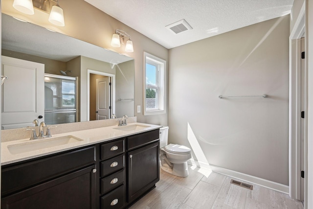 bathroom featuring toilet, hardwood / wood-style floors, a shower with door, vanity, and a textured ceiling