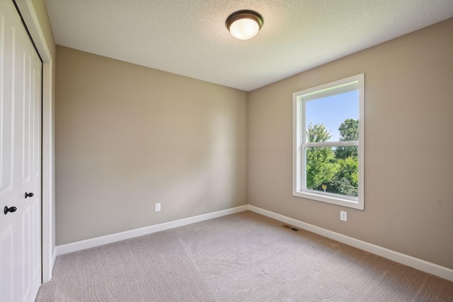 empty room with a textured ceiling and light colored carpet