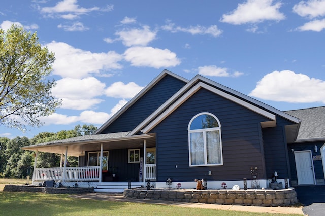 view of front of property featuring a front yard, roof with shingles, and covered porch