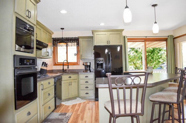 kitchen with a sink, tasteful backsplash, black appliances, under cabinet range hood, and stainless steel counters