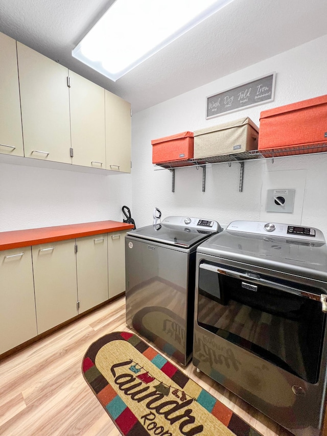 clothes washing area featuring washing machine and clothes dryer, cabinet space, and light wood-style floors