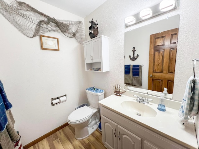 bathroom with vanity, toilet, a textured wall, and wood finished floors