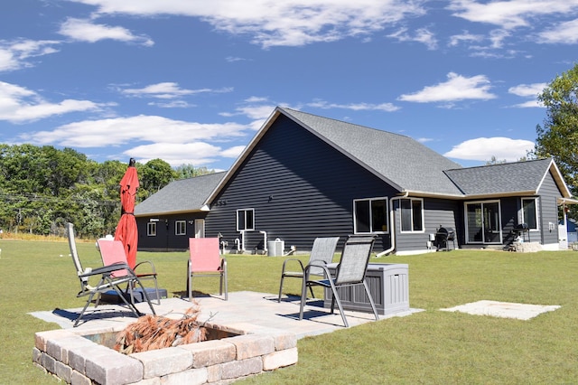 rear view of property featuring a yard, a shingled roof, a patio, and a fire pit