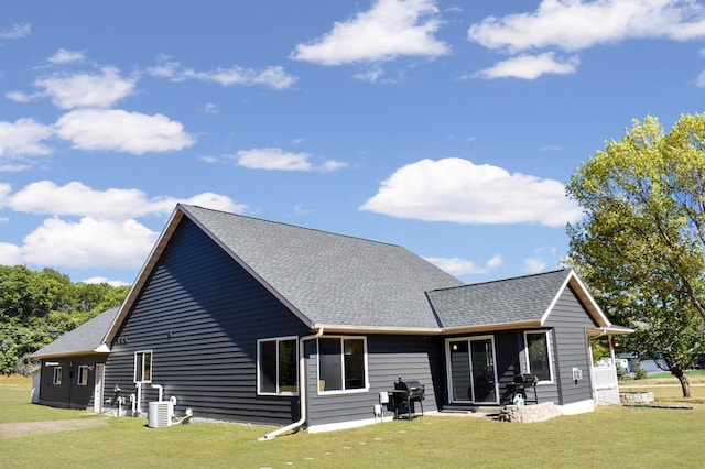 rear view of house featuring roof with shingles, a lawn, and central AC