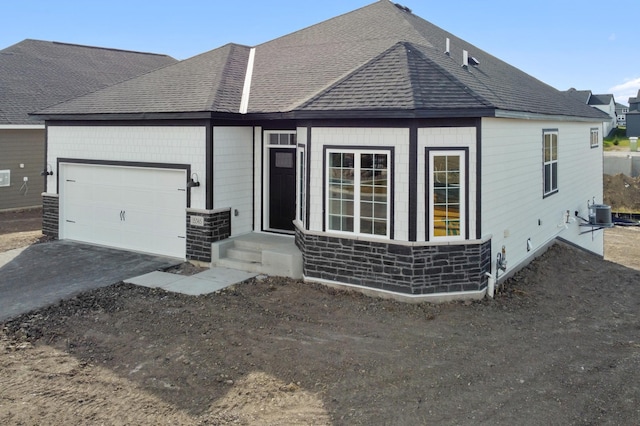 ranch-style home featuring a garage, stone siding, aphalt driveway, and roof with shingles