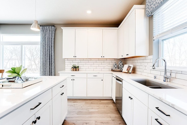 kitchen featuring stainless steel dishwasher, sink, white cabinetry, light hardwood / wood-style flooring, and decorative light fixtures