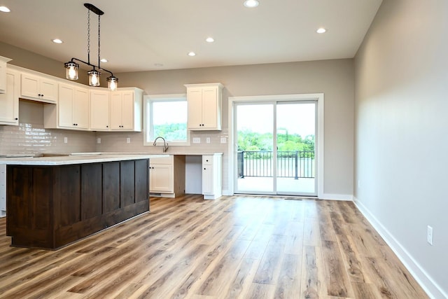 kitchen with light hardwood / wood-style floors, tasteful backsplash, sink, hanging light fixtures, and white cabinetry