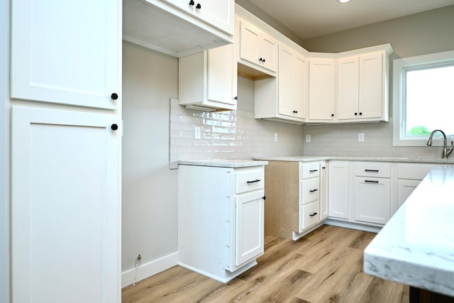 kitchen with light stone countertops, light hardwood / wood-style flooring, tasteful backsplash, and white cabinetry