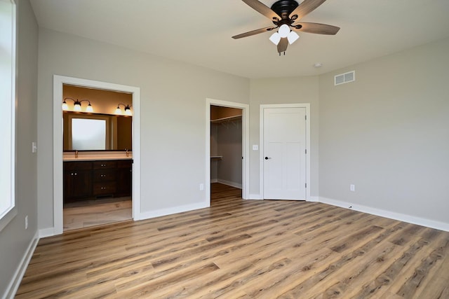 unfurnished bedroom with light wood-type flooring, ceiling fan, a spacious closet, a closet, and connected bathroom