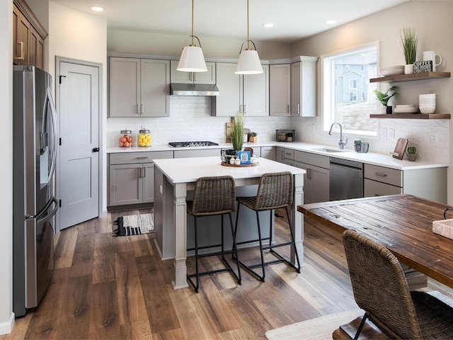 kitchen with appliances with stainless steel finishes, decorative light fixtures, a kitchen island, and dark hardwood / wood-style flooring